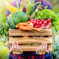 Woman holding freshly harvested vegetables in a wooden crate