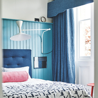 A blue bedroom with full length curtains hung at the window with a matching pelmet above