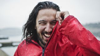 A man wearing a red rain jacket laughs in the rain