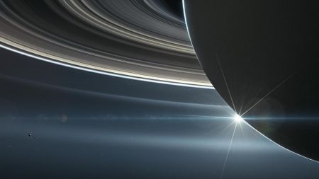 an illustration showing a close up of Saturn and its rings with a small spacecraft orbiting around it