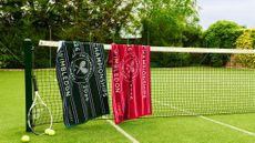 Christy x Wimbledon championship towels pictured in a grassy, tree-lined tennis court, draped overtop of the net