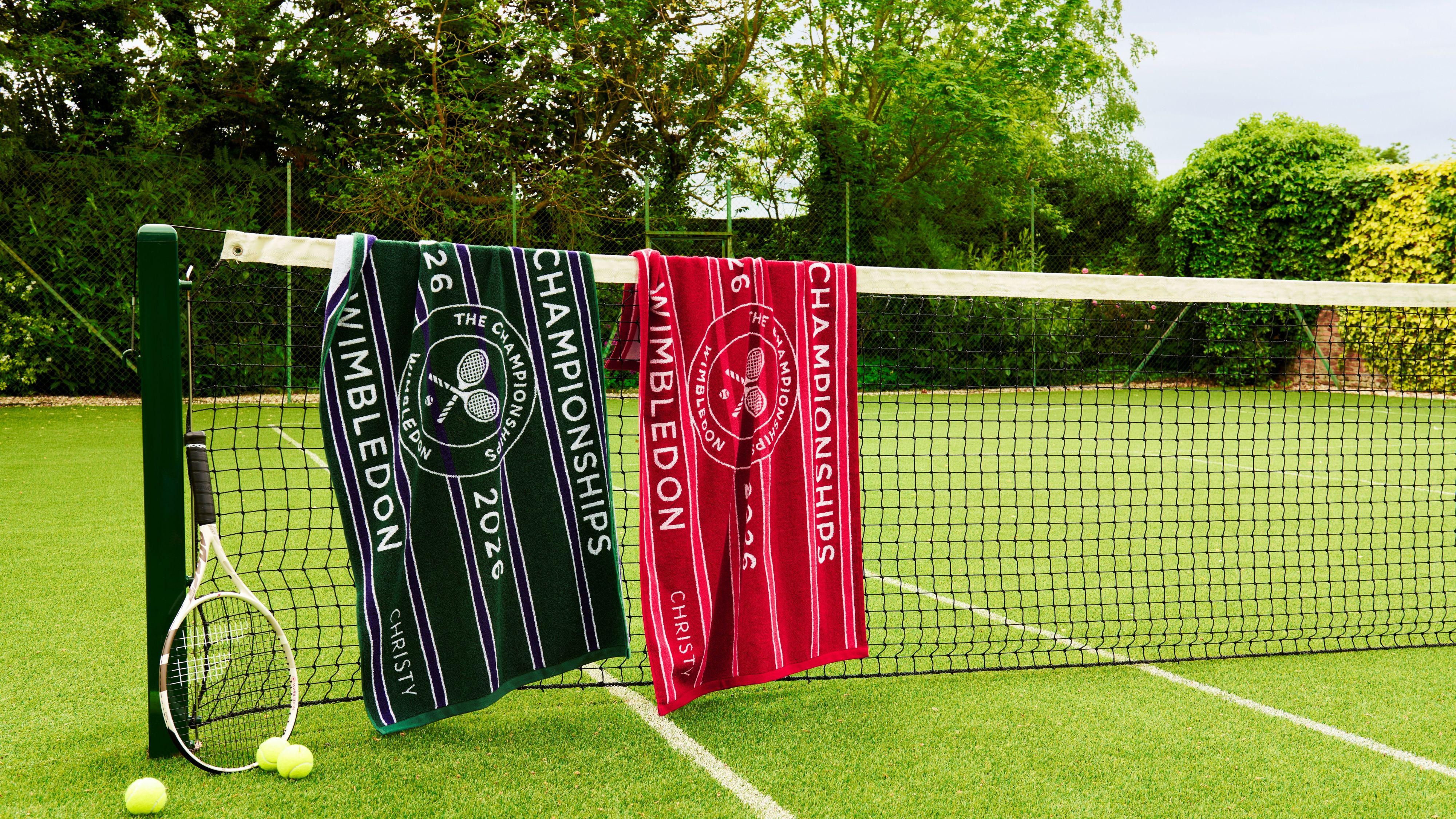 Christy x Wimbledon championship towels pictured in a grassy, tree-lined tennis court, draped overtop of the net