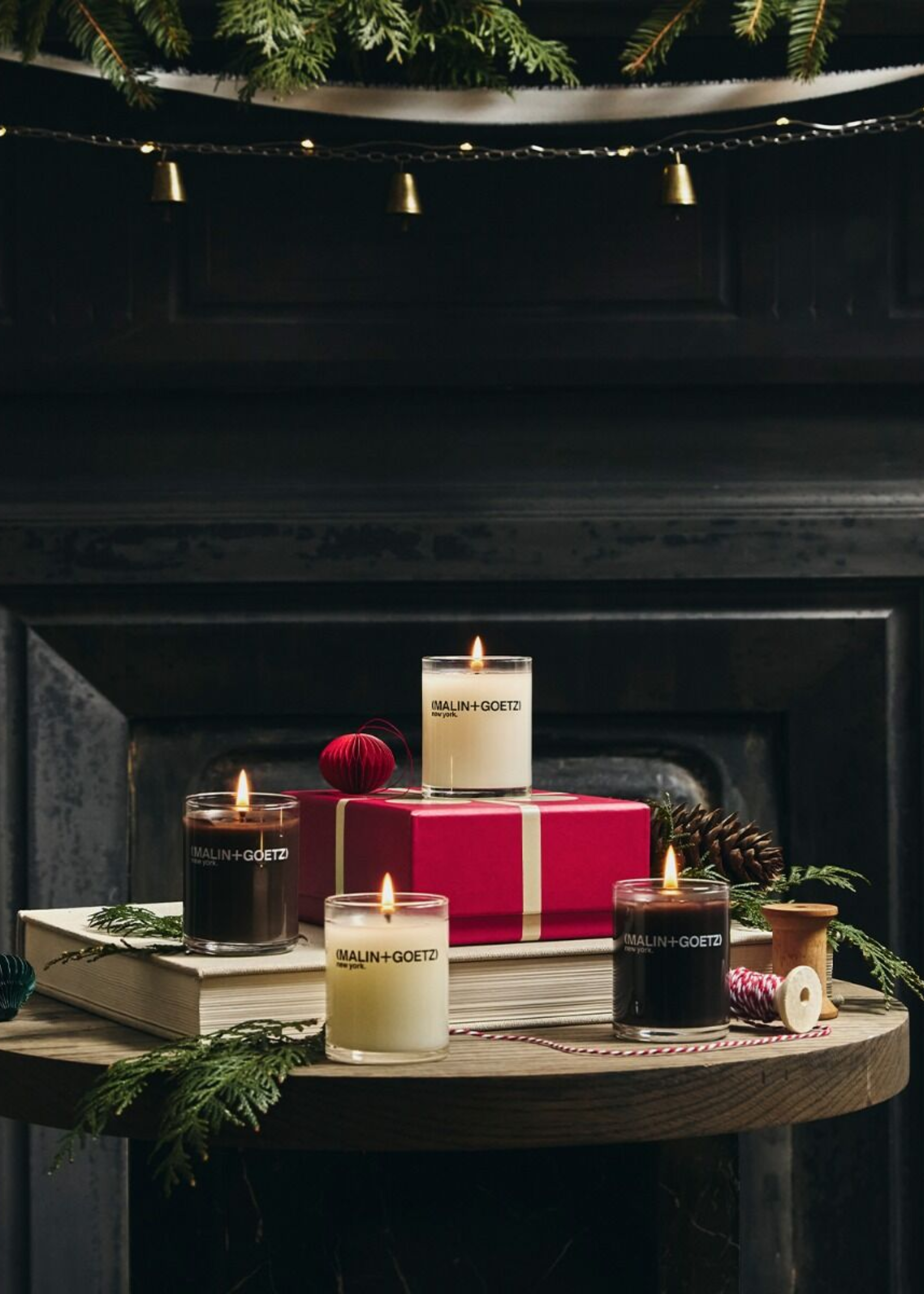 A wood table in front of a fireplace with glass candles and fir garlands