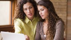 A mother helps her college-bound daughter on a laptop at the kitchen table.