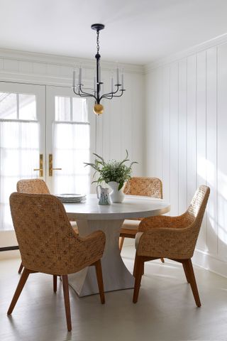 round dining table and wicker chairs in room white walls and french windows