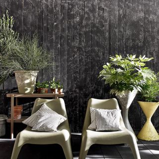 Two garden chairs with cushions in front of plants and black garden fence