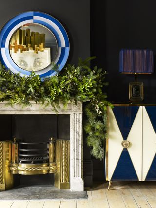 A fireplace decorated with a Christmas garland next to a geometric black and white painted cabinet