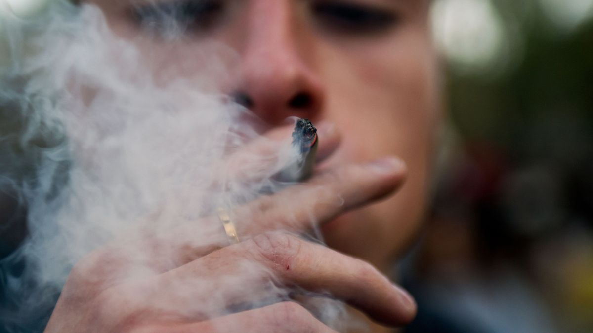 closeup of a man smoking a joint outdoors, as he blows out a large plume of smoke