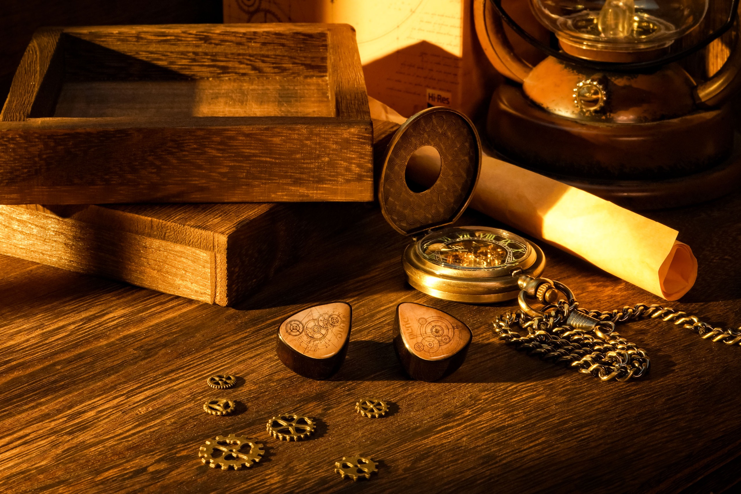 A pair of Dunu DaVinci Vitruvian earbuds, with sepia faceplates etched with clockwork gear drawings, sits on a dark wooden desk beside an open pocket watch, a rolled parchment and scattered brass cogs