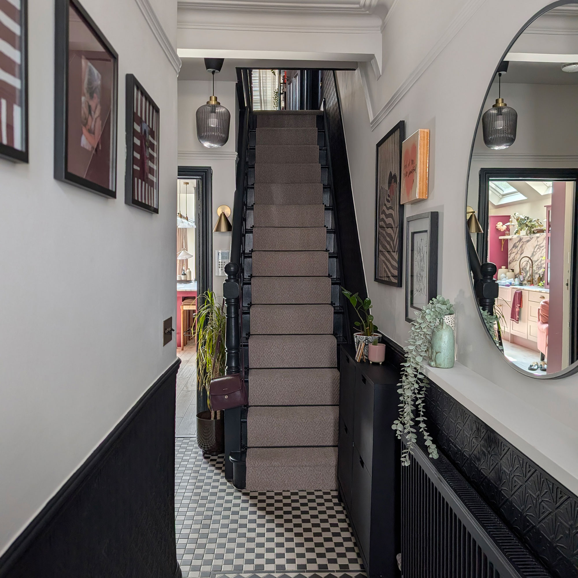 Hallway with lower half of walls painted blue-black, and top half white. Matching blue-black banisters. Grey carpet runner on stairs. Black and white chequered flooring