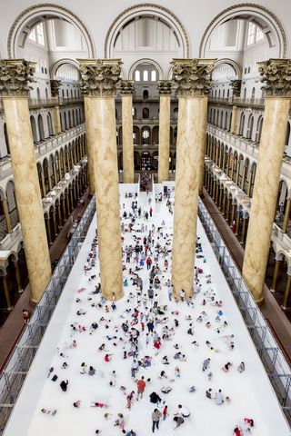 Aerial view of people playing in indoor beach display between huge marble columns in museum