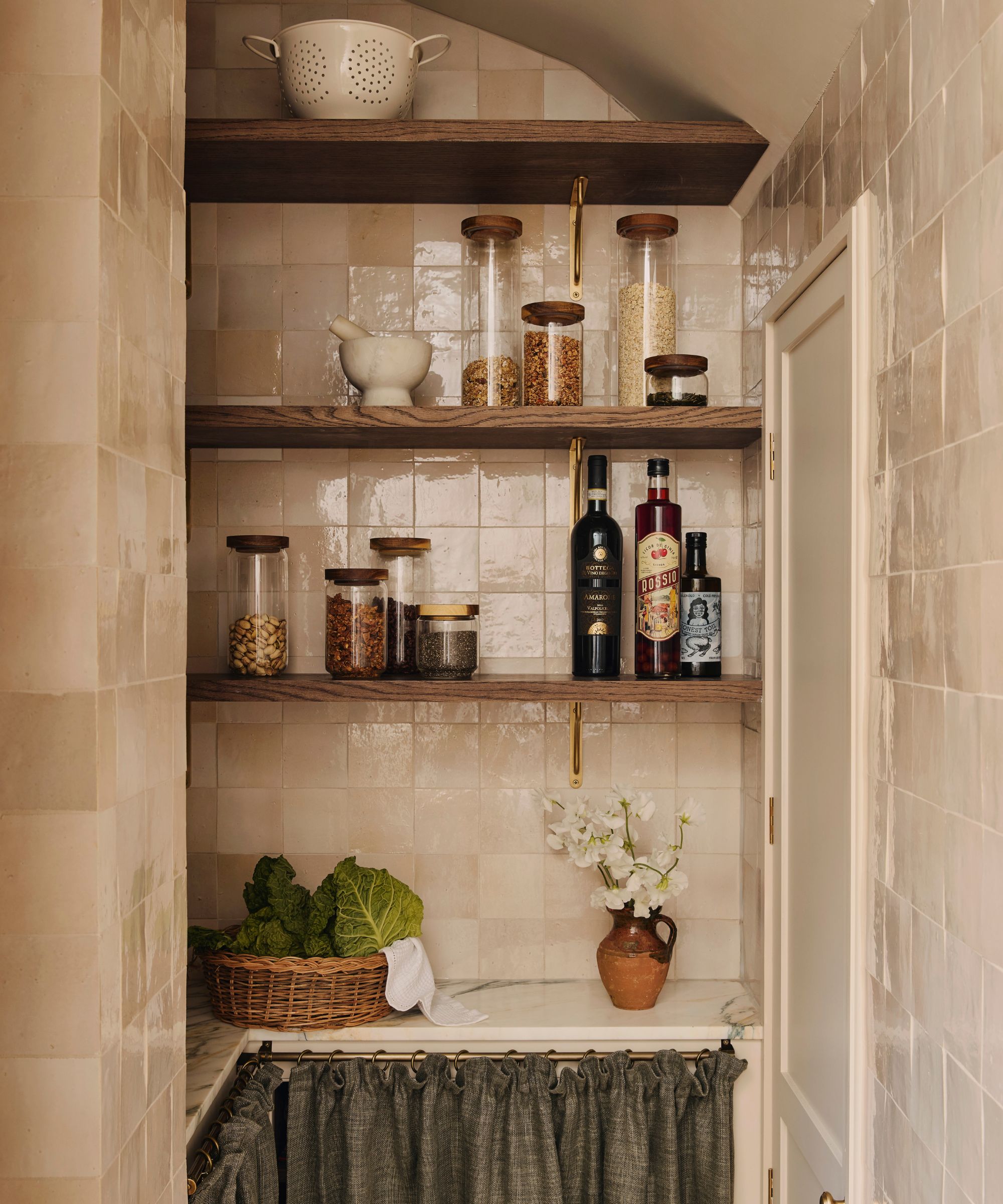 Cream tiled pantry with shelves of glass storage containers and condiments and skirted storage