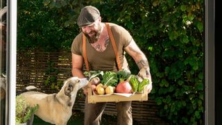 Man holding a vegetable basket while a dog sniffs it