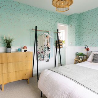 green bedroom with wooden chest and clothes rail with white bedding