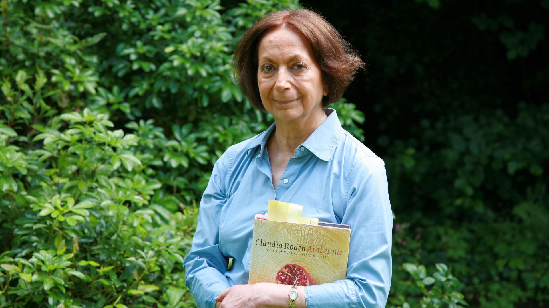 Claudia Roden holds a book in a garden
