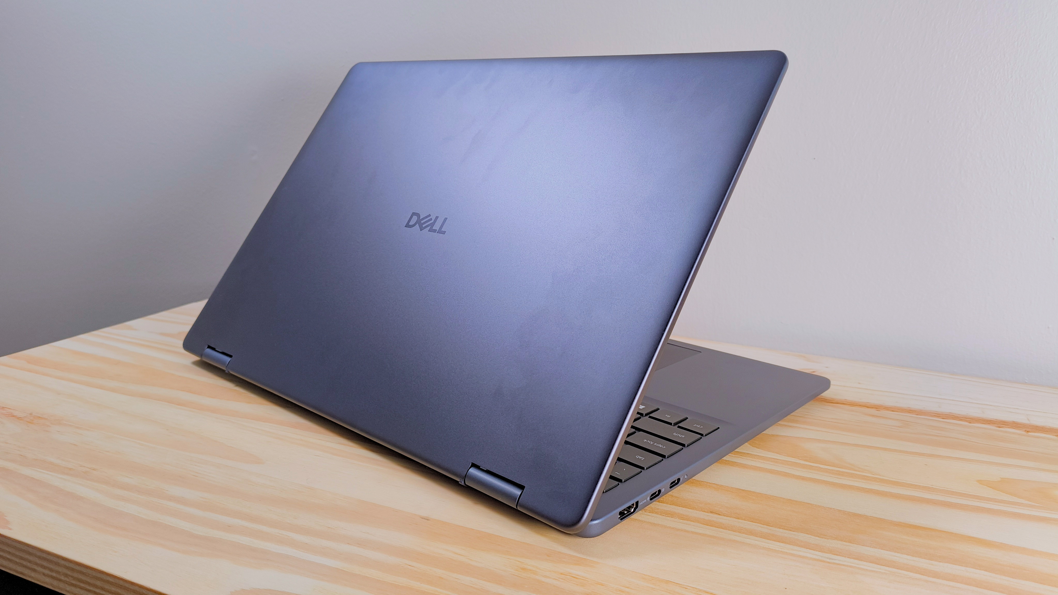 The Dell 16 Plus 2-in-1 with lid open seen from behind on a wood table