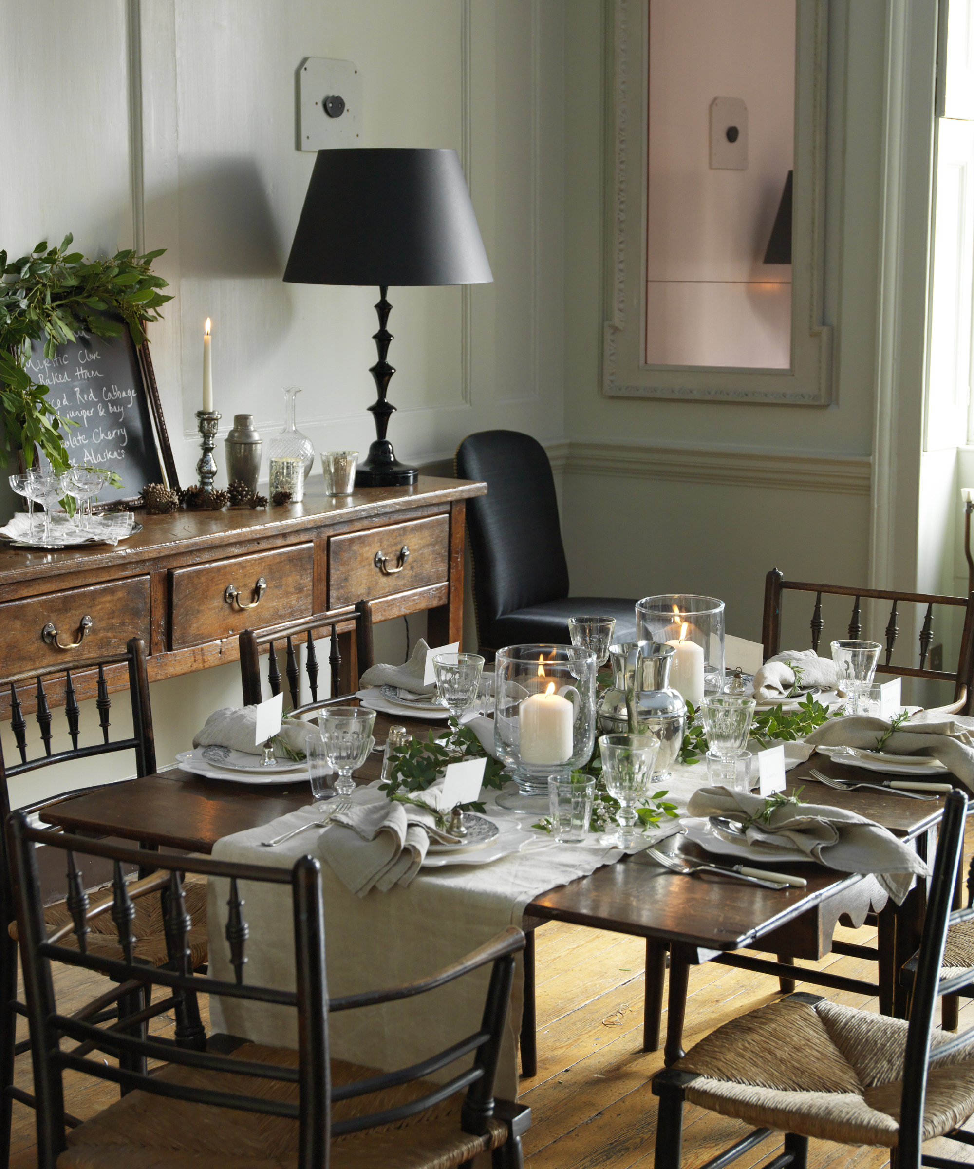 A dining table decor idea with a taupe runner and foliage decor with hurricane candles