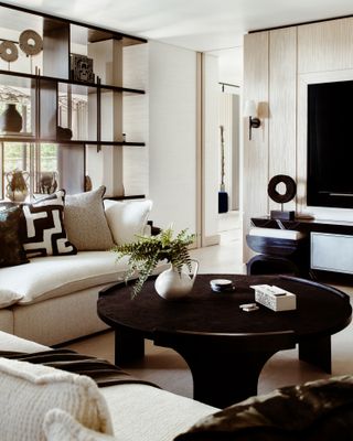 Living space with sectional couch in neutral, black round coffee table and shelving