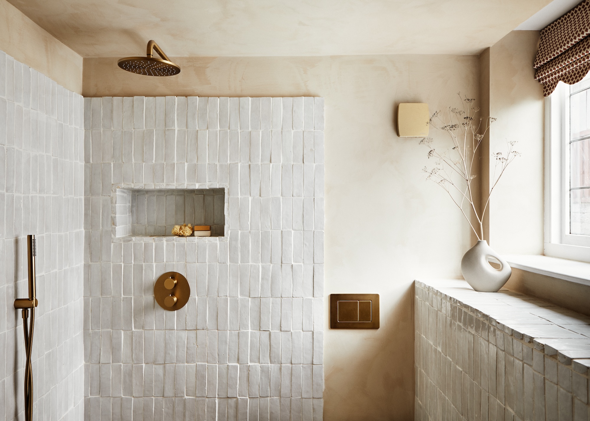 a modern rustic bathroom with plastered walls and simple white tiles with masses of texture plus old gold shower fittings