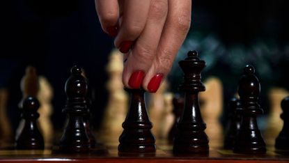 A hand moving a chess piece on a board