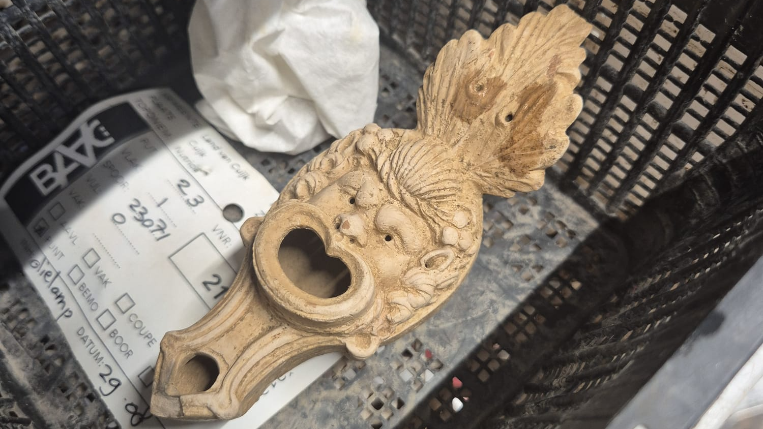 cleaned Roman oil lamp in a black basket with a white label underneath