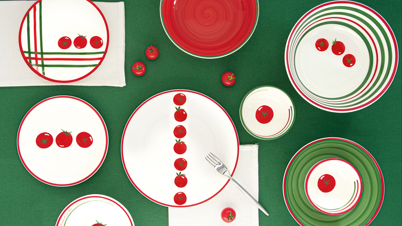 Collection of tomato themed bowls and plates on a green tablecloth.