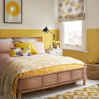 Half-painted yellow bedroom wall with patterned blind, bedspread and rug