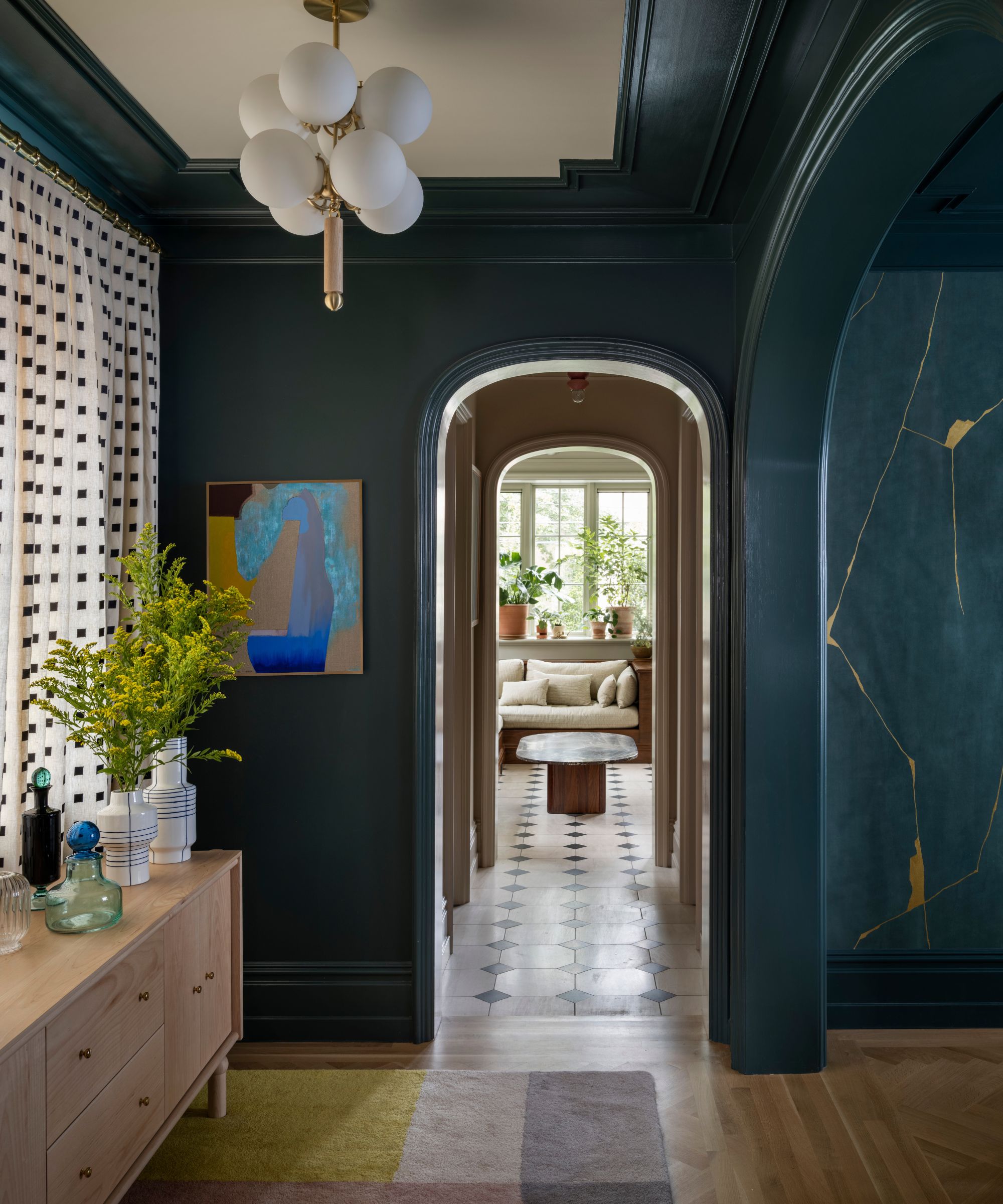 A dining room foyer with dark green walls and trim, arched doorways, a light wooden sideboard, a white ceiling, and a modern circular ceiling light.
