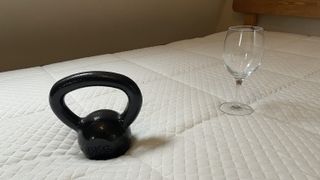 Image shows a black 6kg weight dropped roughly 8 inches from an empty wine glass placed on top of the Nectar Mattress during a motion isolation test