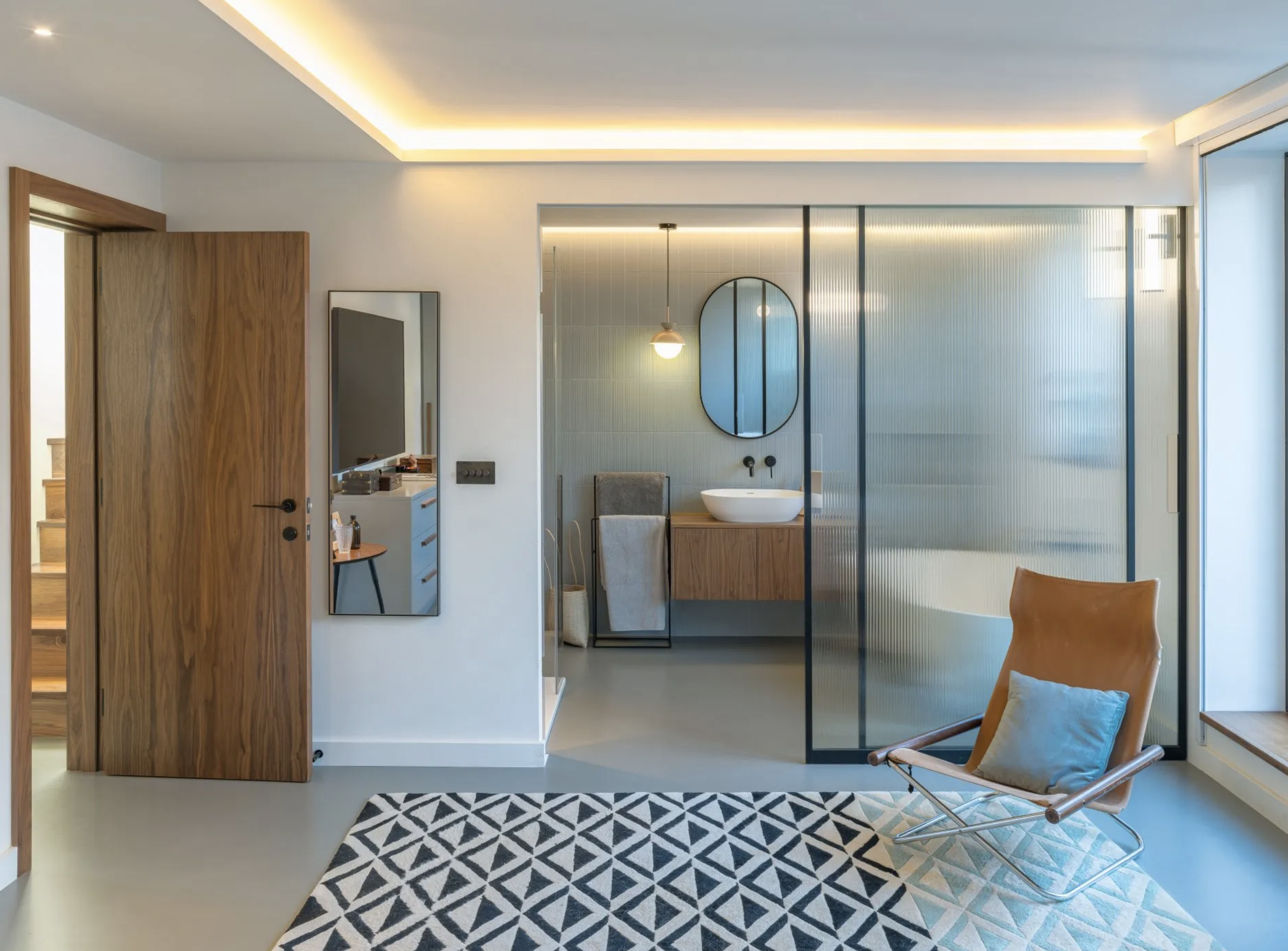 A bedroom with an ensuite featuring midcentury furniture and a frosted glass wall and door