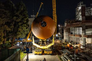 nose-on view of a horizontally aligned orange fuel tank, being held by a crane at night