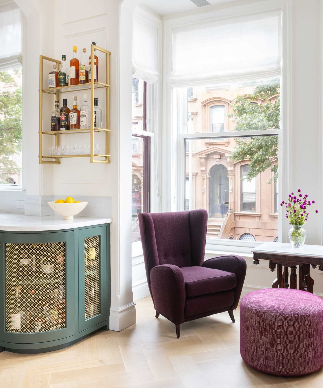 A brownstone living room with a green home bar, purple armchair, and hardwood floors