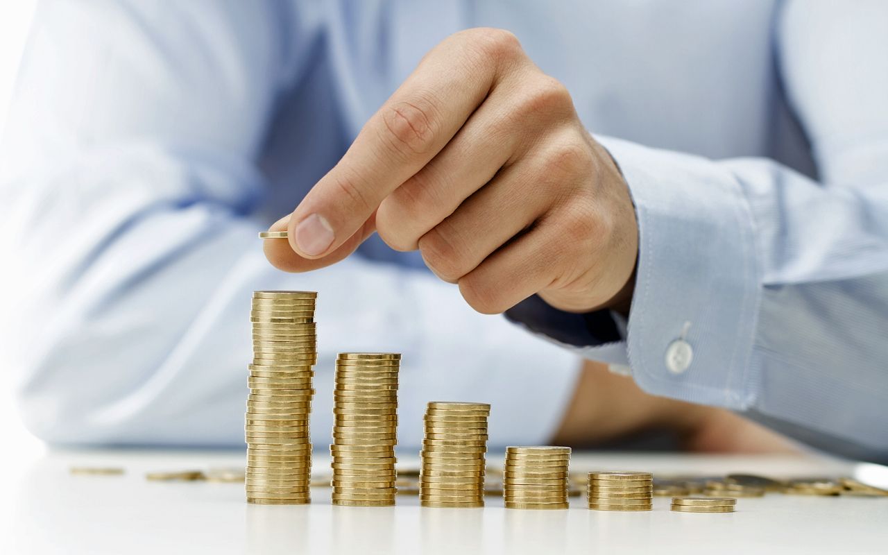 Close up of male hand stacking gold coins into increasing columns