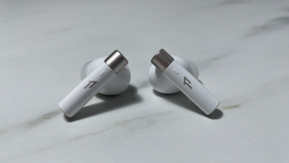 The back of the 1More PistonBuds Pro Q30 earbuds, showing the silver-tipped white posts, with a small raised touch-control area and the 1More logo in silver.