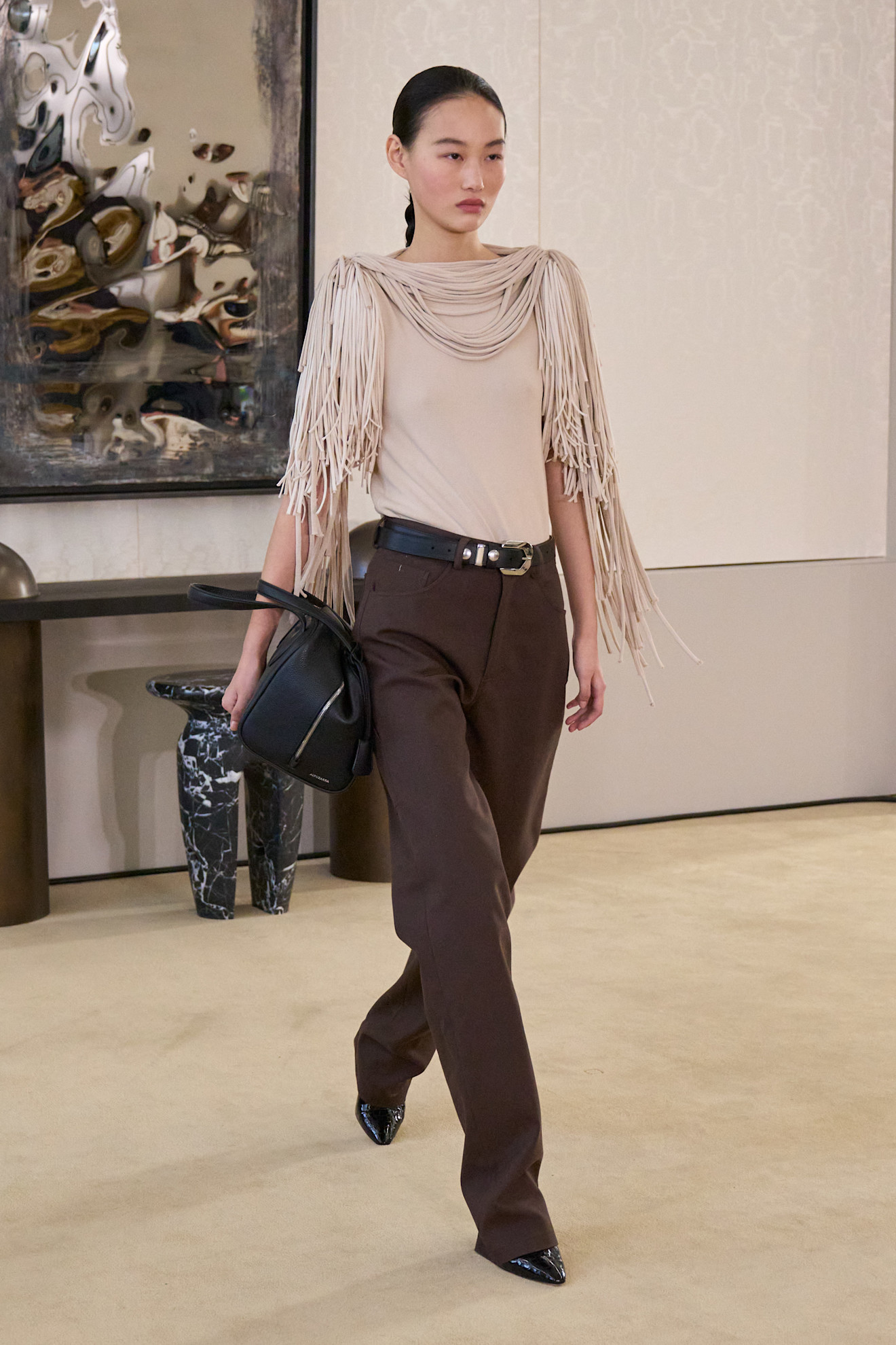 A fall/winter 2026 runway model wearing chocolate-brown trousers.
