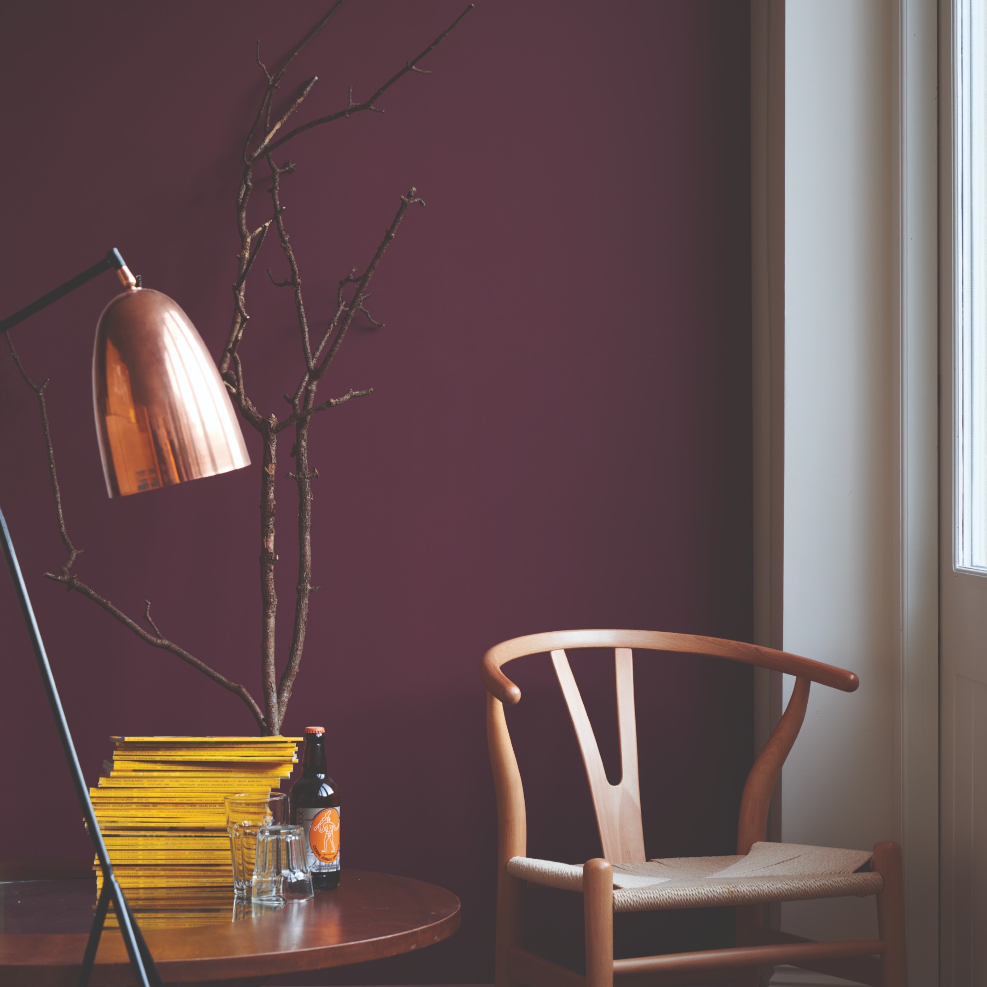 A wishbone chair with a coffee table and a floor lamp against a burgundy wall painted in Farrow &amp;amp; Ball's Preference Red
