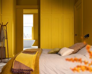 bedroom with bright yellow built-in wardrobes, neutral bedding with yellow throw blanket and doorway leading to bathroom