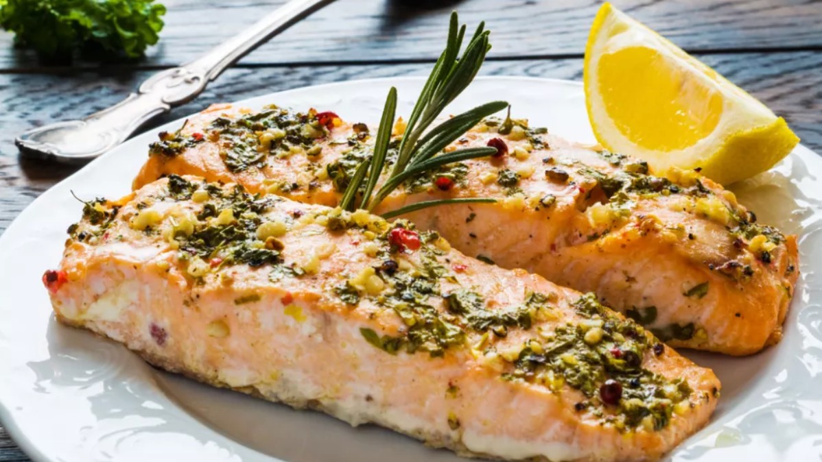 Cooked salmon on plate with rosemary and lemon wedge