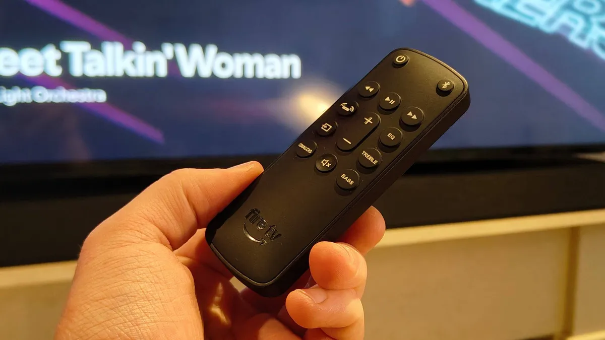 The Amazon Fire TV Soundbar Plus remote in front of a TV.