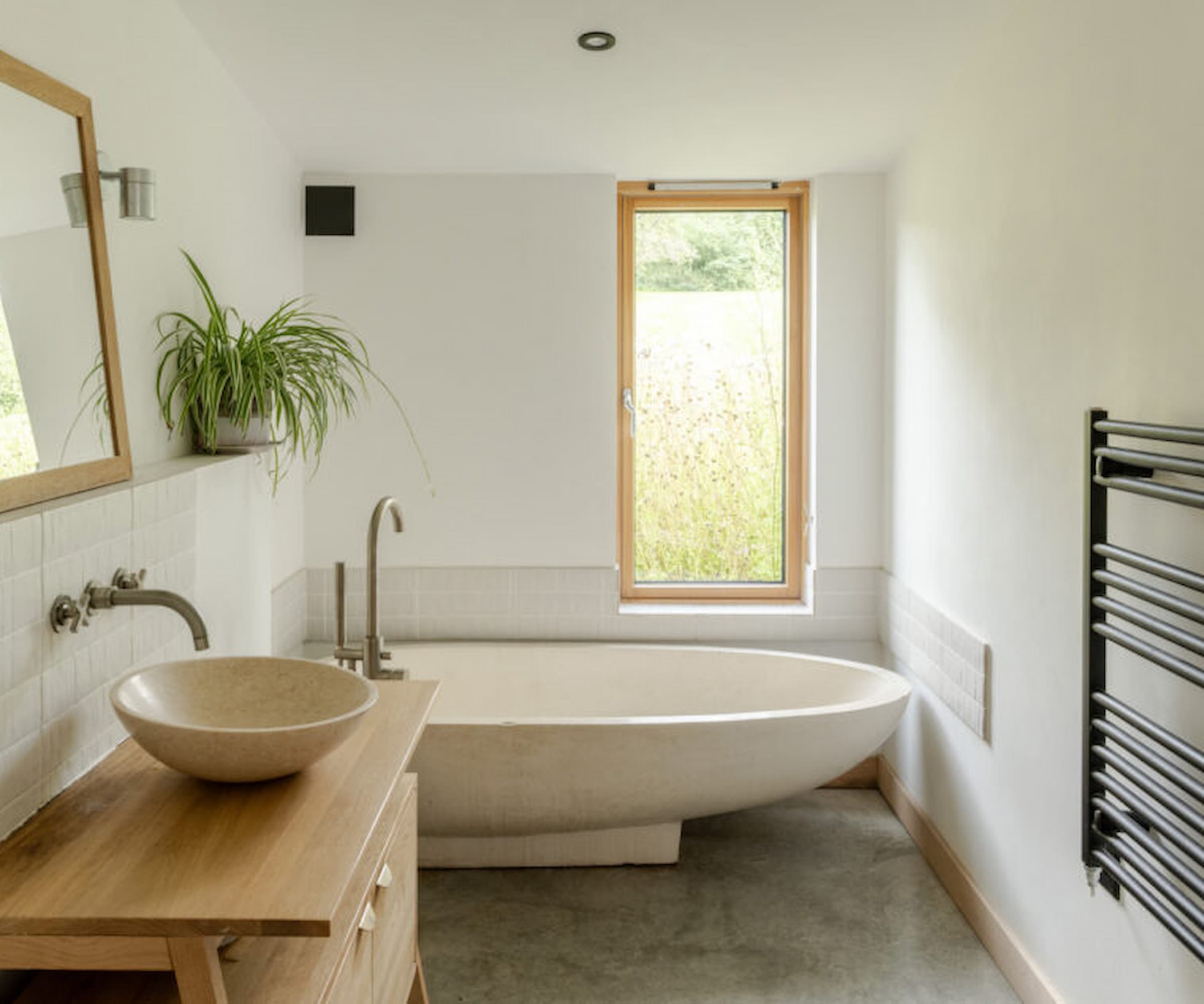 A low bath in a bathroom with a spider plant and a wooden basin stand for the sink