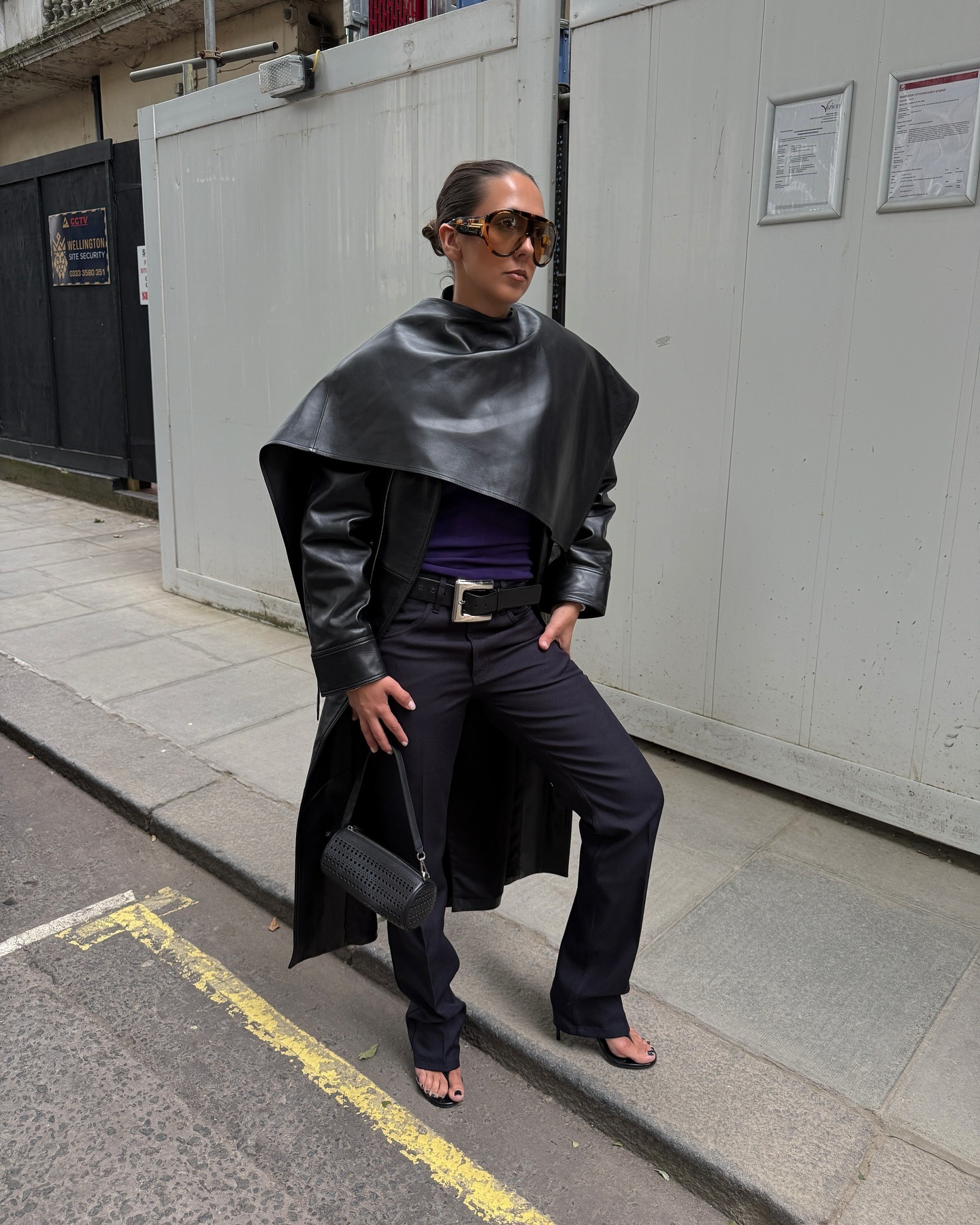 Hanna MW wearing a leather cape jacket, black pants, and stretch thong sandals.