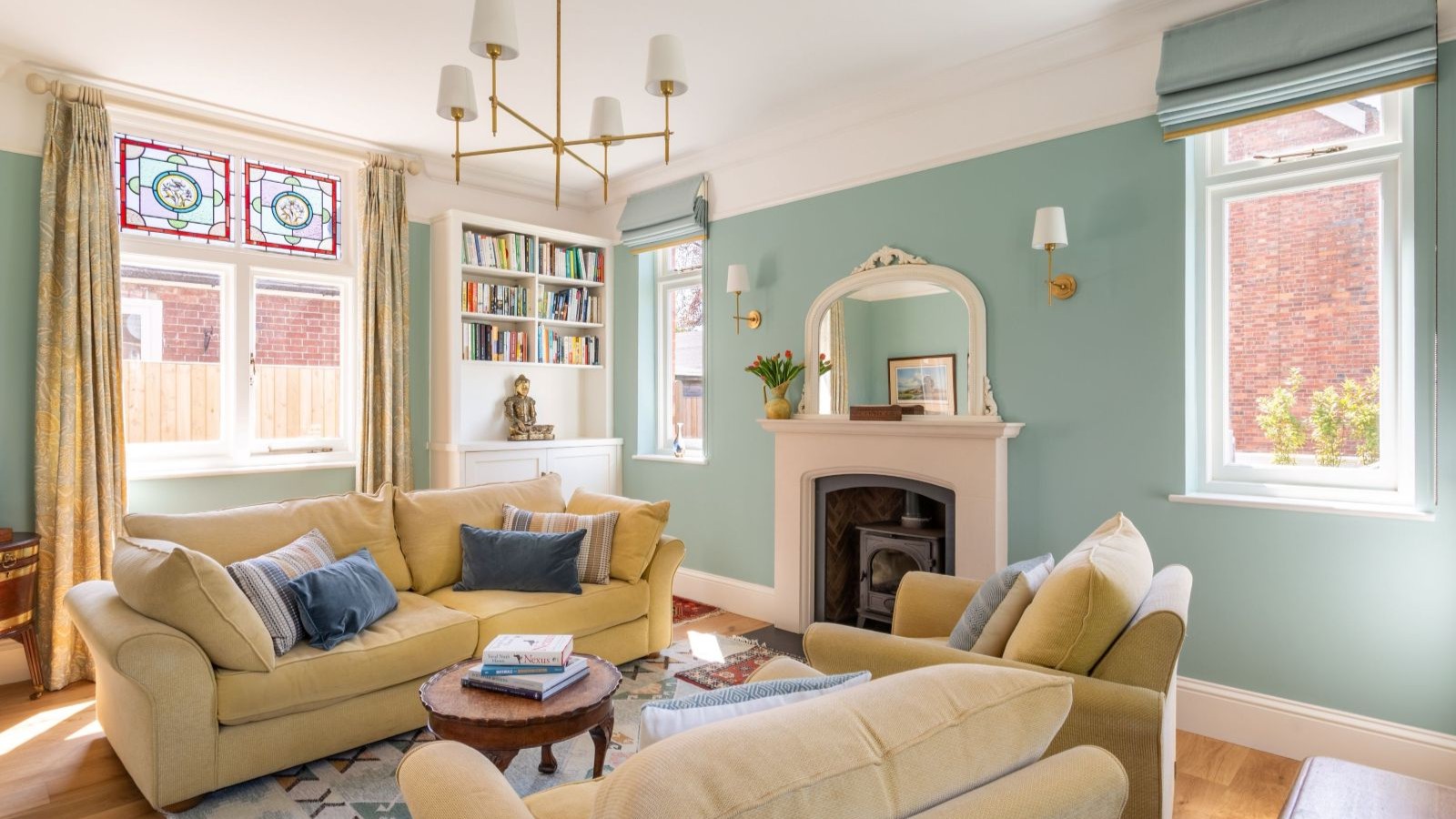 A duck egg blue living room with yellow velvet sofas and stained glass windows above normal glazing