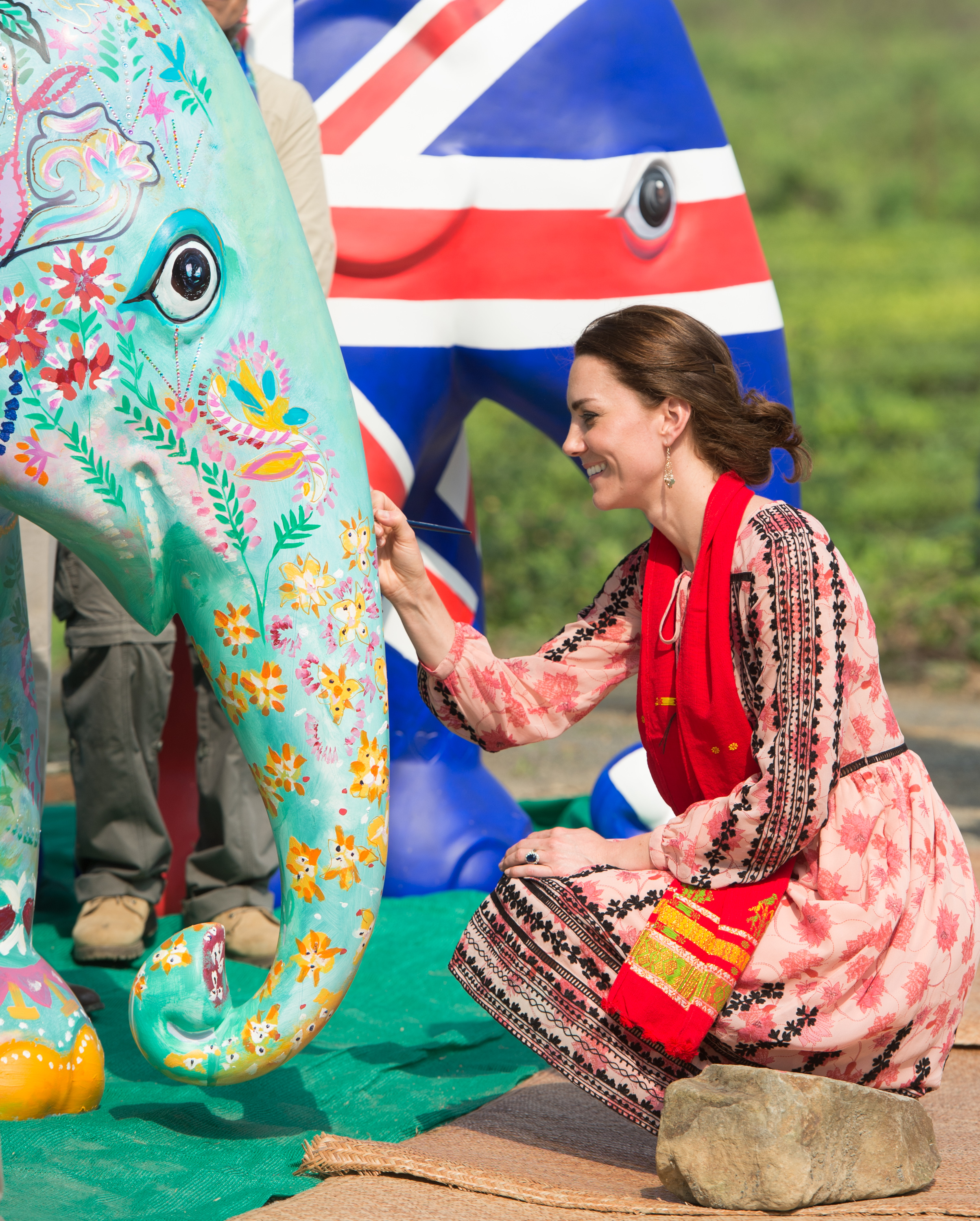 Princess Kate kneeling down in a pink dress painting a colorful elephant statue