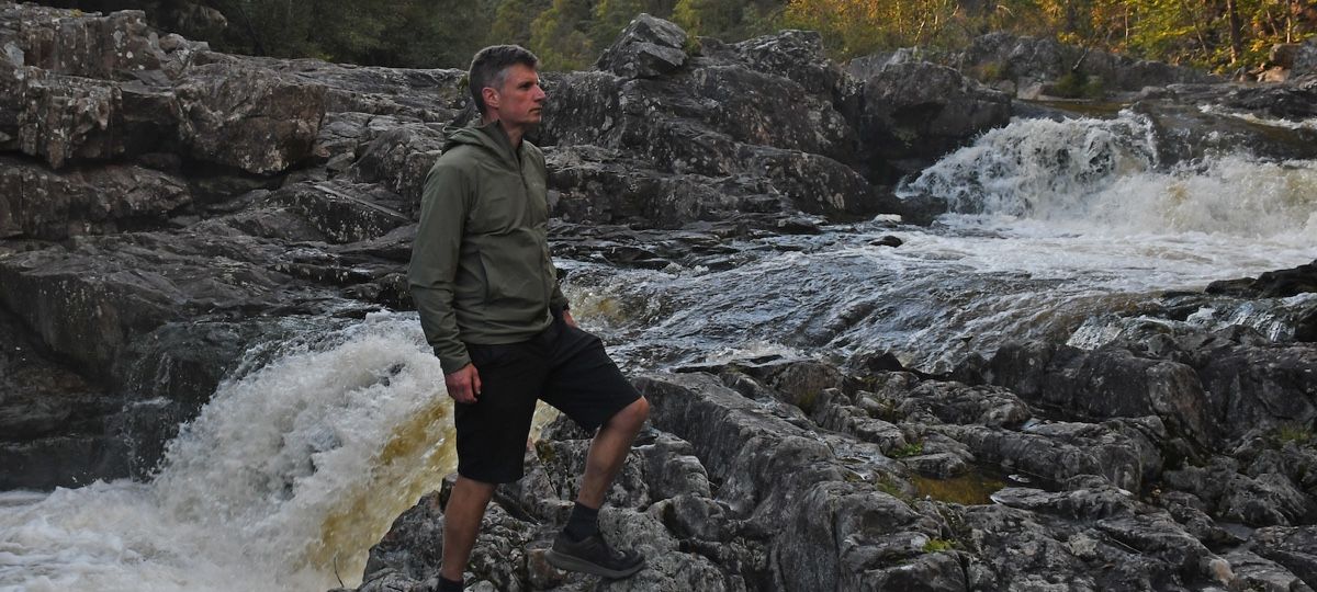 Hiker next to stream wearing a Montane Khamsin Hooded Softshell Jacket