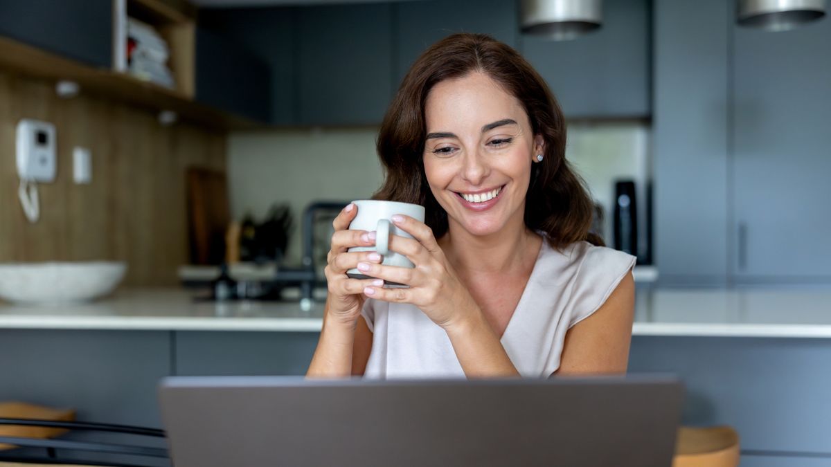 Woman drinking coffee and looking happily at laptop