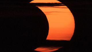 The sun takes on the appearance of a crescent moon as the moon appears to take a "bite" out of the sun's orange disk bathed in clouds.