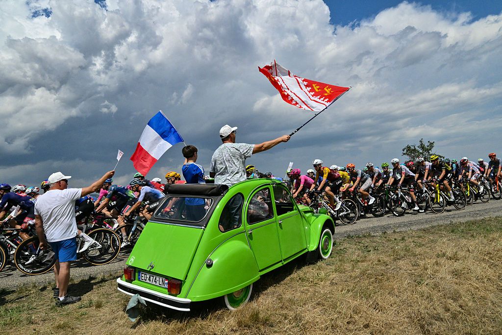 Spectators atop a Citroen 2CV wave flags as the pack of riders (peloton) cycles past during the 14th stage of the 113th edition of the Tour de France cycling race, 155,3 km between Mulhouse and Le Markstein in the Vosges mountains, on July 18, 2026. (Photo by Jeff PACHOUD / AFP)