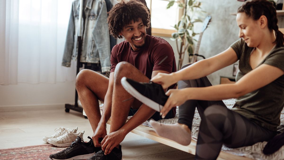 A young couple sitting on the edge of their bed, putting on trainers