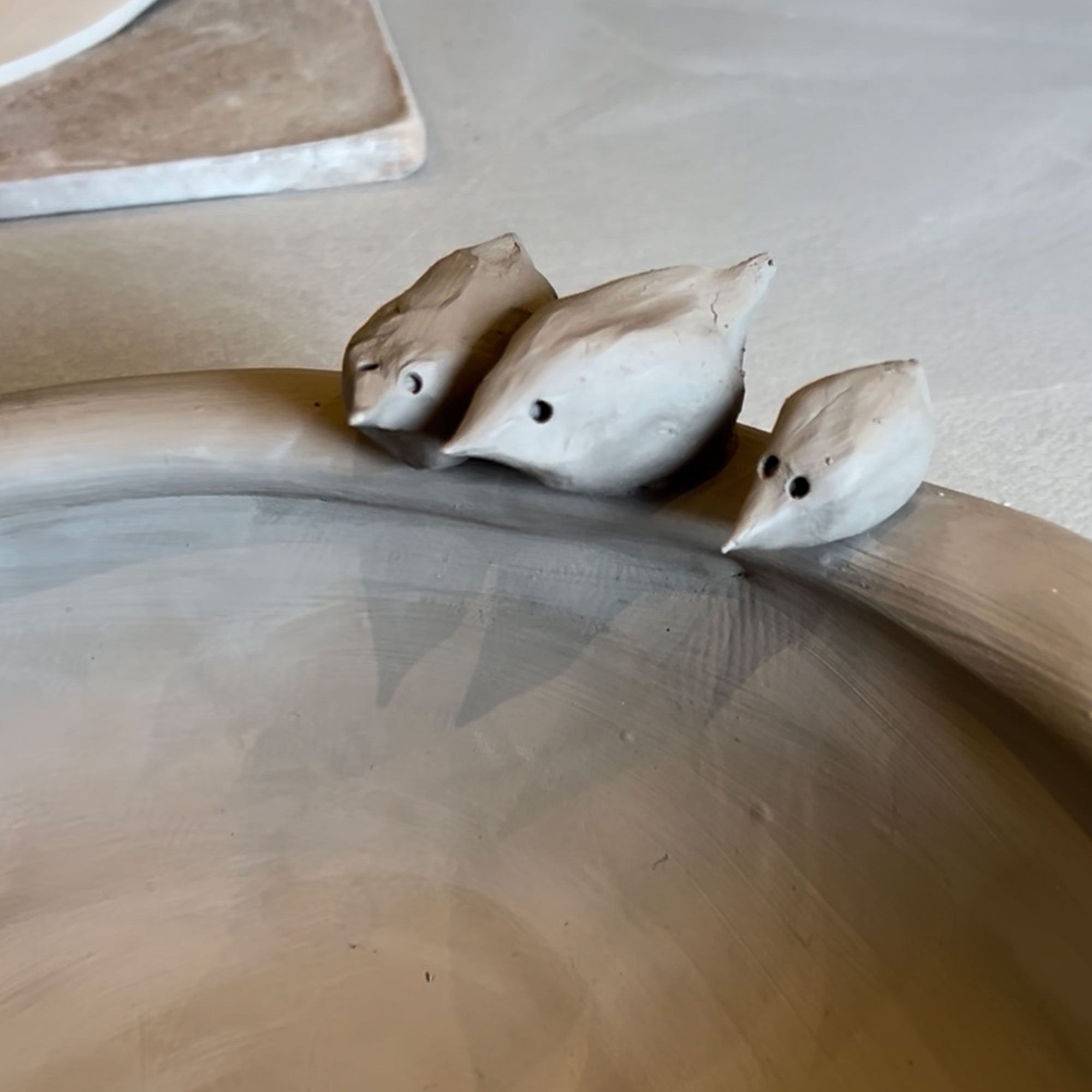 Clay bowl with three birds perched on rim, pre-firing
