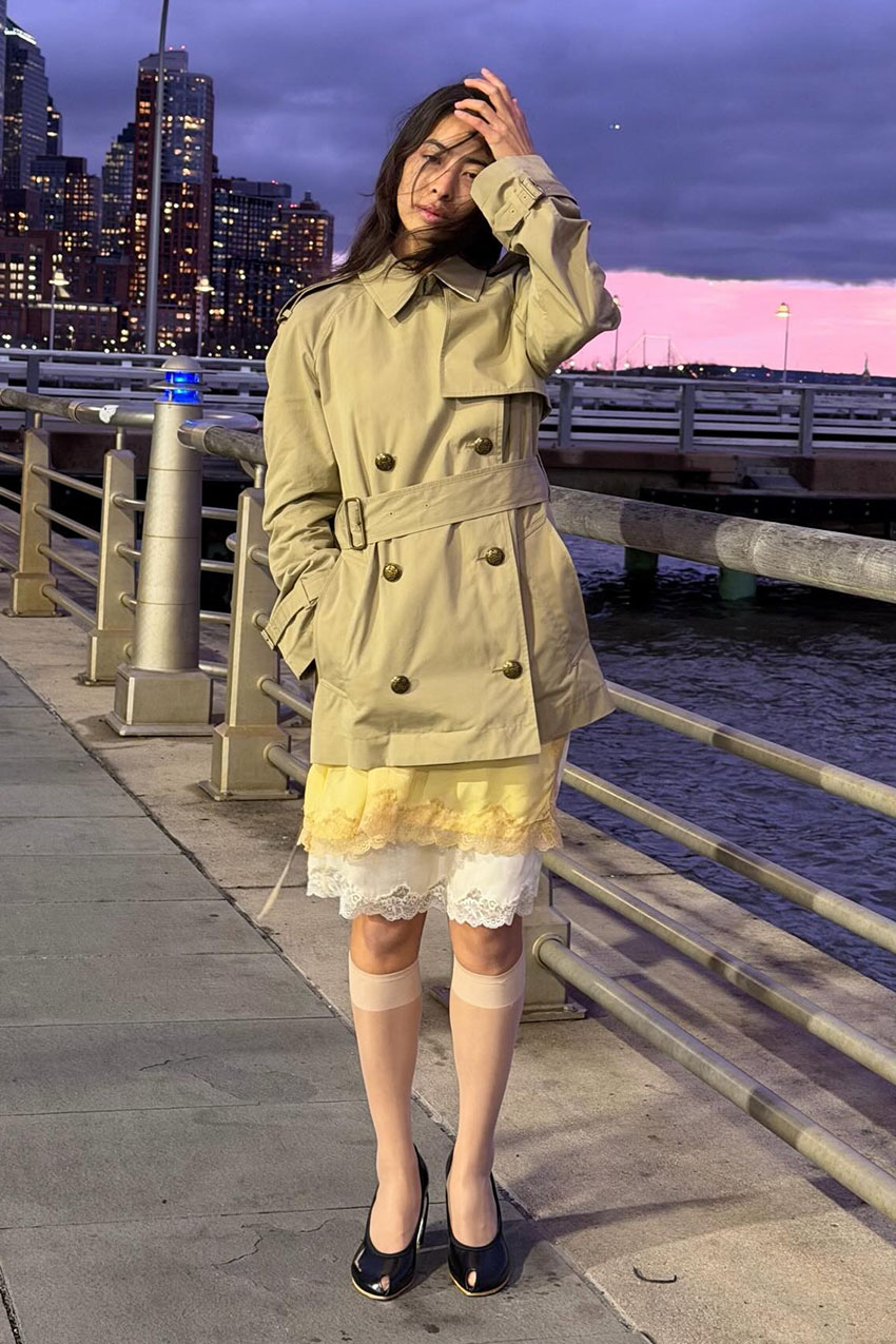 A woman wearing a trench coat and lace-trim skirt.
